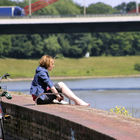 Frau sitzt neben ihrem Fahrrad auf einer Mauer und betrachtet den Rhein