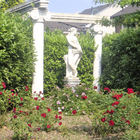Zwischen Säulen stehende Sandsteinskulptur, davor blühen rote Rosen